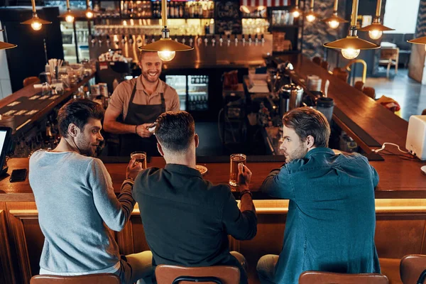 Top view of relaxed young men in casual clothing drinking beer while sitting in the pub — Stock Photo, Image