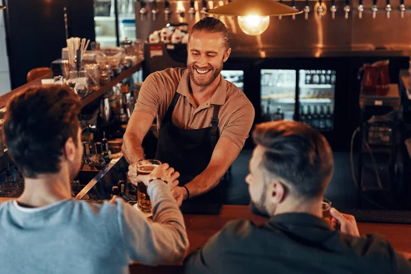 Top view of bartender serving beer to young men while standing at the bar counter in pub — 图库照片