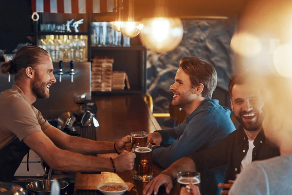 Top view of smiling young men in casual clothing drinking beer and bonding together while sitting in the pub — Fotografia de Stock