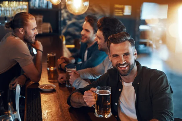 Top view of carefree young men in casual clothing drinking beer and bonding together while sitting in the pub — Fotografia de Stock