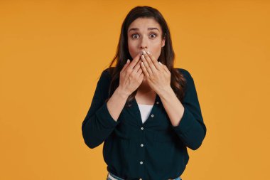 Surprised young woman in casual clothing using covering mouth with hands