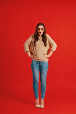 Full length of shocked young woman in casual clothing making a face and looking at camera