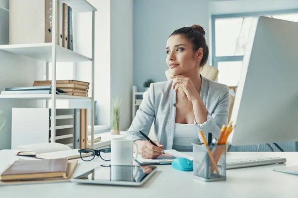 Beautiful young woman in smart casual wear looking away and smiling while working in the office — Zdjęcie stockowe