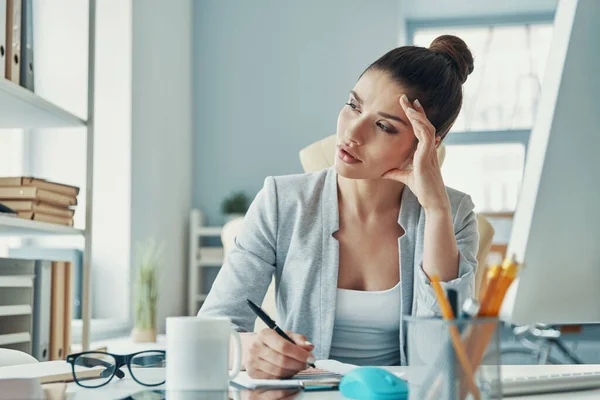 Thoughtful young woman in smart casual wear looking away while working in the office — Foto Stock