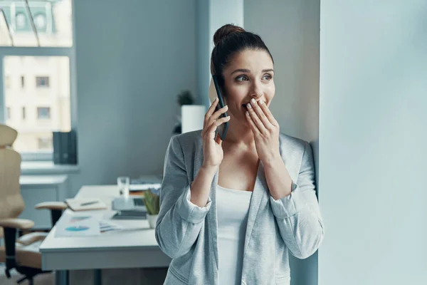 Beautiful young woman in smart casual talking on the phone and covering mouth — 图库照片