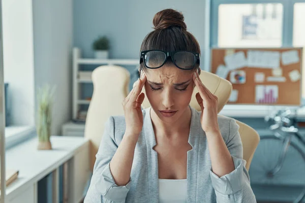 Stressed young woman in smart casual wear keeping head in hands while sitting in the office — 图库照片