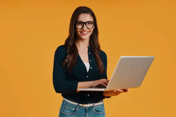 Happy young woman in smart casual clothing using laptop and smiling — Φωτογραφία Αρχείου