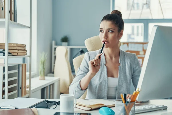Thoughtful young woman in smart casual wear looking away while sitting in the office — Foto de Stock