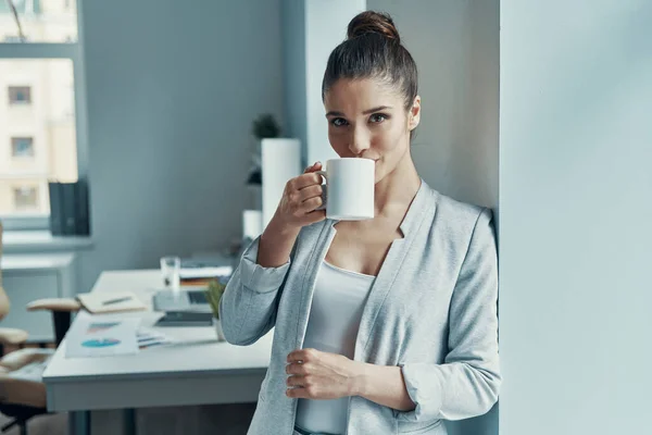 Beautiful young woman in smart casual wear looking at camera and holding a cup — Stockfoto