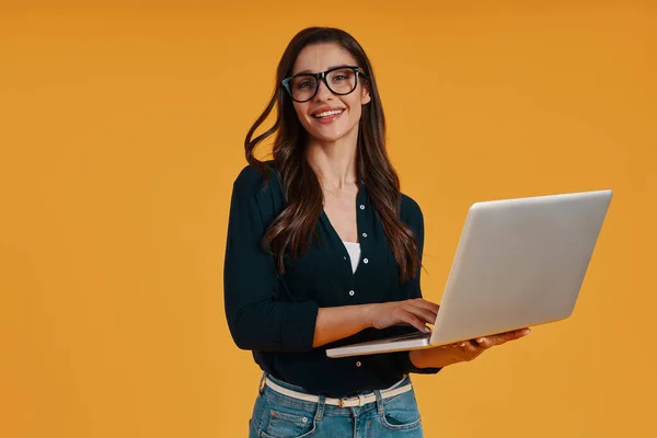 Happy young woman in smart casual clothing using laptop and smiling — ストック写真