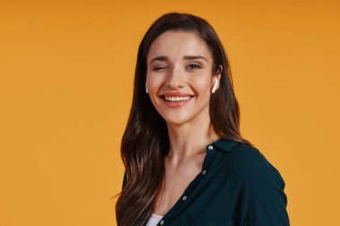 Happy young woman in casual clothing listening music and winking