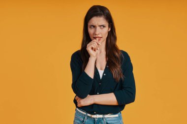 Thoughtful young woman in casual looking away while standing against yellow background