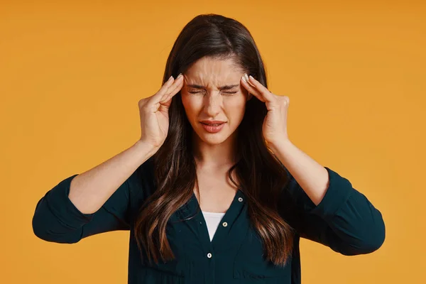 Young woman in casual clothing suffering from headache while standing against yellow background — Foto de Stock