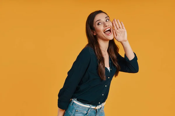 Playful young woman in casual clothing making a face while standing against yellow background — ストック写真