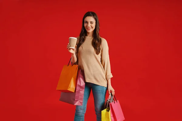 Beautiful young woman in casual clothing carrying shopping bags and winking — стоковое фото