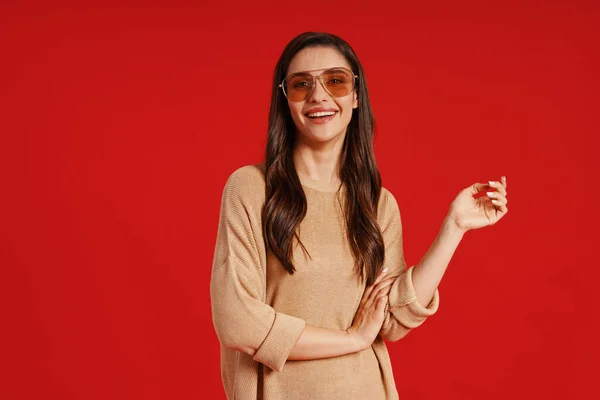 Beautiful young woman in casual clothing smiling while standing against red background — Stock Fotó