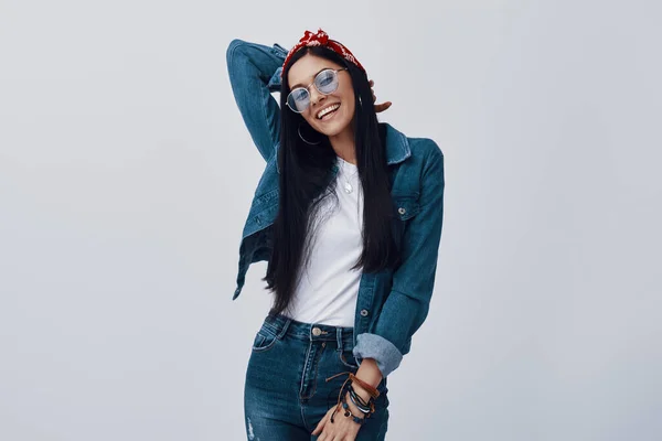 Attractive young woman in eyewear and bandana smiling while standing against grey background — Stock Photo, Image