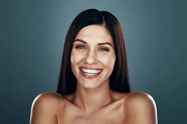 Beautiful young woman smiling while standing against grey background — Stock Photo, Image