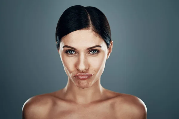 Belle jeune femme faisant un visage et regardant la caméra tout en se tenant debout sur fond gris — Photo