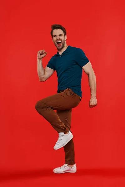 Comprimento total de jovem feliz em casual desgaste gestos contra fundo vermelho — Fotografia de Stock