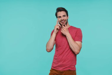 Yakışıklı, güler yüzlü, sıradan giyinmiş, akıllı telefondan konuşan bir adam.