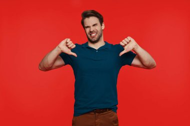 Sıradan giyinmiş genç adam kameraya bakıyor ve baş parmaklarını aşağı gösteriyor.