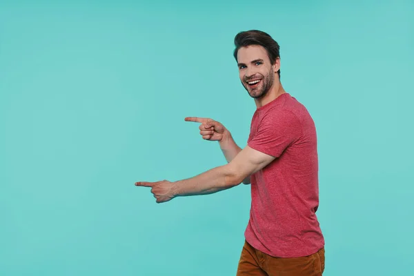 Handsome young smiling man in casual clothing looking at camera and pointing away — Stock Photo, Image