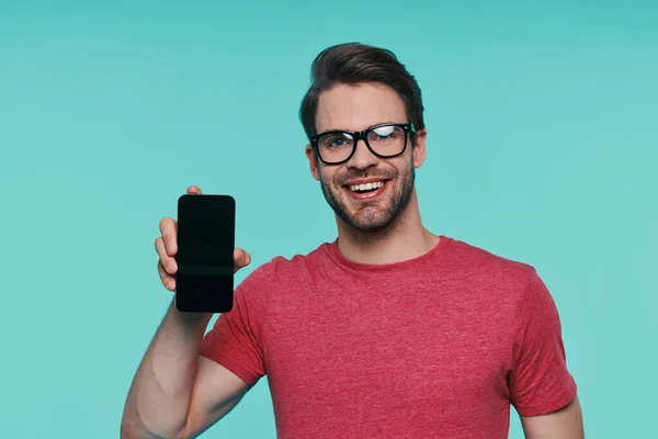 Портрет красивого молодого человека в очках, показывающего свой смартфон и улыбающегося — стоковое фото
