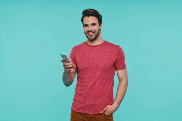 Bello giovane uomo sorridente in abbigliamento casual in possesso di smart phone — Foto Stock