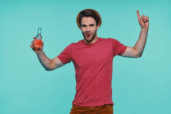 Knappe jonge glimlachende man in casual kleding holding fles met drinken en gebaren — Stockfoto