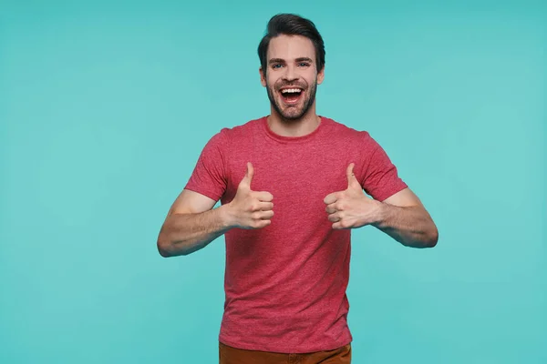 Bonito jovem em roupas casuais olhando para a câmera e mostrando seus polegares para cima — Fotografia de Stock