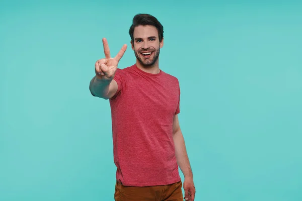 Guapo joven sonriente hombre apuntando cámara mientras está de pie sobre fondo azul —  Fotos de Stock