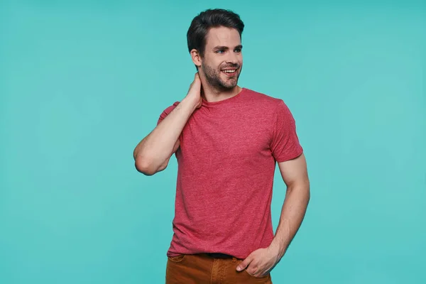 Guapo joven con ropa casual mirando hacia otro lado y sonriendo mientras está de pie sobre fondo azul — Foto de Stock