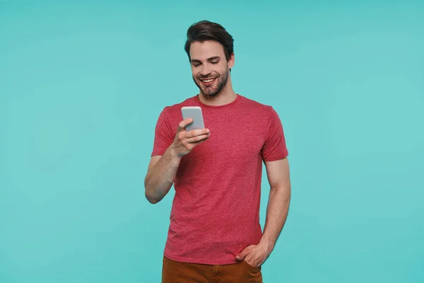 Bello giovane uomo sorridente in abbigliamento casual sms su smart phone — Foto Stock