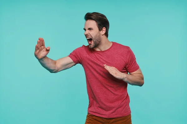 Furioso jovem sorrindo homem em roupas casuais gestos contra fundo azul — Fotografia de Stock