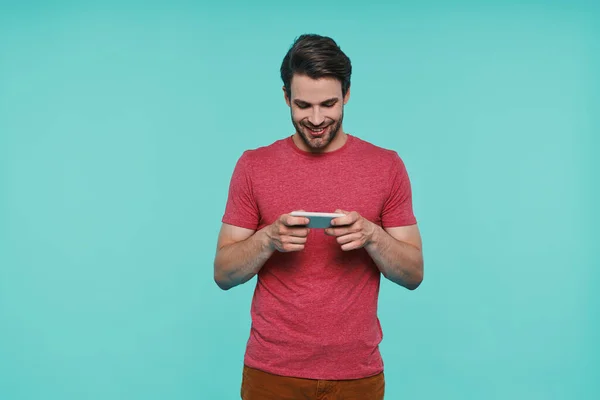 Bello giovane uomo sorridente in abbigliamento casual guardando smart phone — Foto Stock