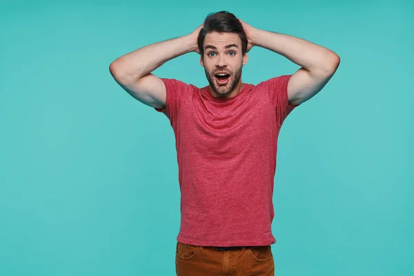 Excited young man in casual clothing looking at camera and holding hands on head — Stock Photo, Image