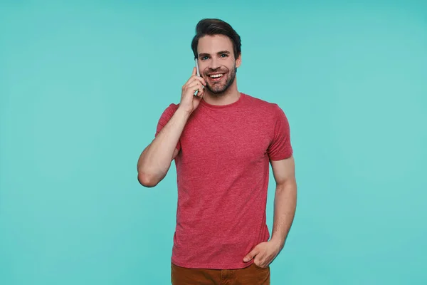 Knappe jonge glimlachende man in casual kleding kijken naar de camera en praten op de smartphone — Stockfoto