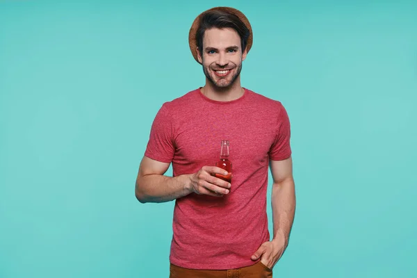 Przystojny młodzieniec w luźnych ciuchach trzyma butelkę z drinkiem i uśmiechem — Zdjęcie stockowe