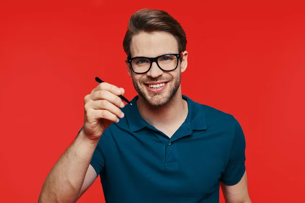 Retrato de un joven guapo en ropa casual mirando a la cámara y sosteniendo la pluma — Foto de Stock