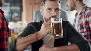 Yakışıklı genç adam barda arkadaşlarıyla vakit geçirirken bira içiyor.