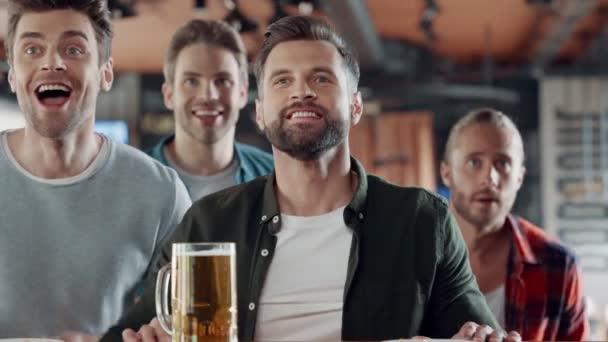 Cheering young men drinking beer and watching sport game in the pub — Stok Video