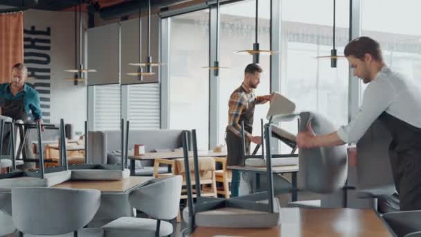 Camareros masculinos en ropa de trabajo protectora arreglando muebles en restaurante — Vídeos de Stock