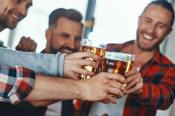 Glada unga män i vardagskläder skålar med öl och ler — Stockfoto