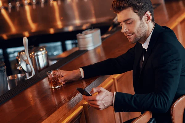 Schöner junger Mann in vollem Anzug mit Smartphone, während er an der Theke im Restaurant sitzt — Stockfoto