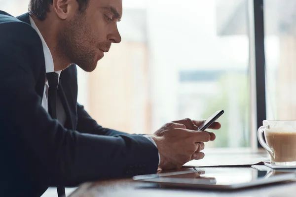 Side view of handsome young man in full suit using smart phone while sitting in the restaurant — Stock Photo, Image