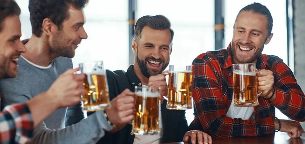 Gelukkig jonge mannen in casual kleding toosten elkaar met bier en glimlachen — Stockfoto