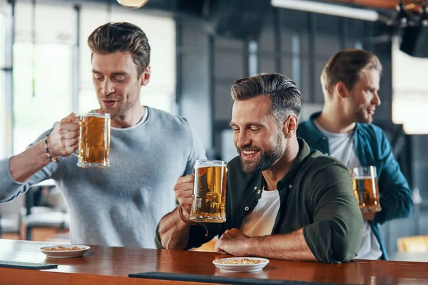 Group of cheerful young men in casual clothing enjoying beer and communicating — 图库照片