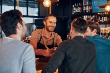 Barın tezgahında genç adamlara bira servisi yapan neşeli bir barmen.
