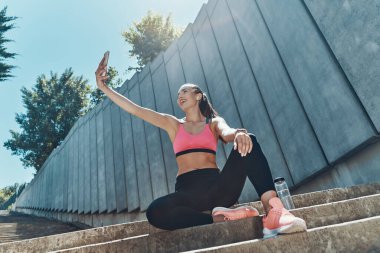 Spor elbiseli güzel bir kadının akıllı telefonuyla selfie çekmesini alçak açıdan izlemek.